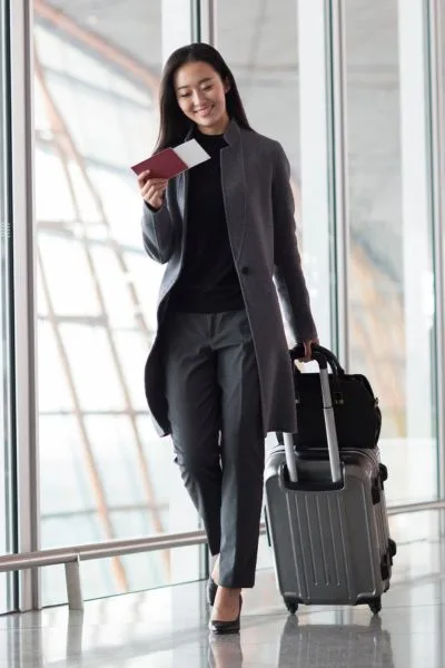 Elegant traveler arriving at the airport with suitcase and passport – luxury airport transfer service on the French Riviera.
