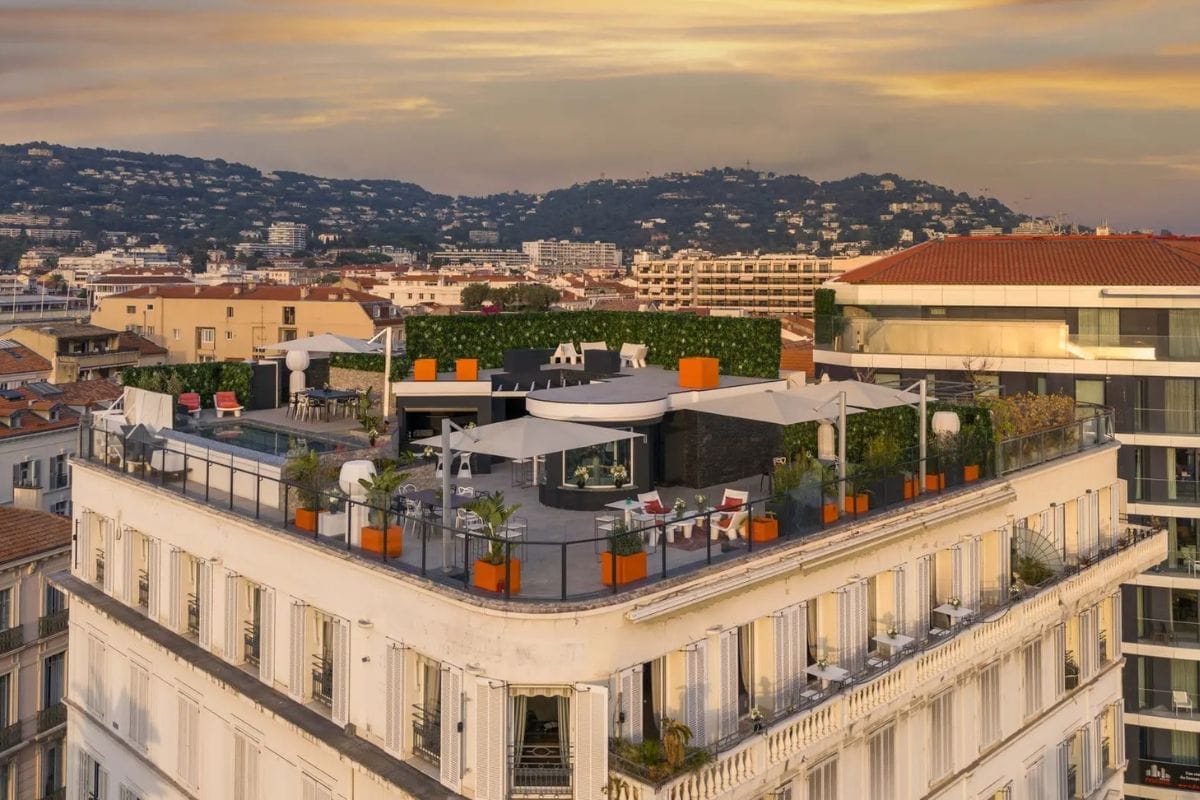 penthouse-le-monroe-cannes-exterior-rooftop-terrace-city-view Penthouse Le Monroe in Cannes featuring a panoramic rooftop terrace with lounge areas, greenery, and sweeping city views at sunset.