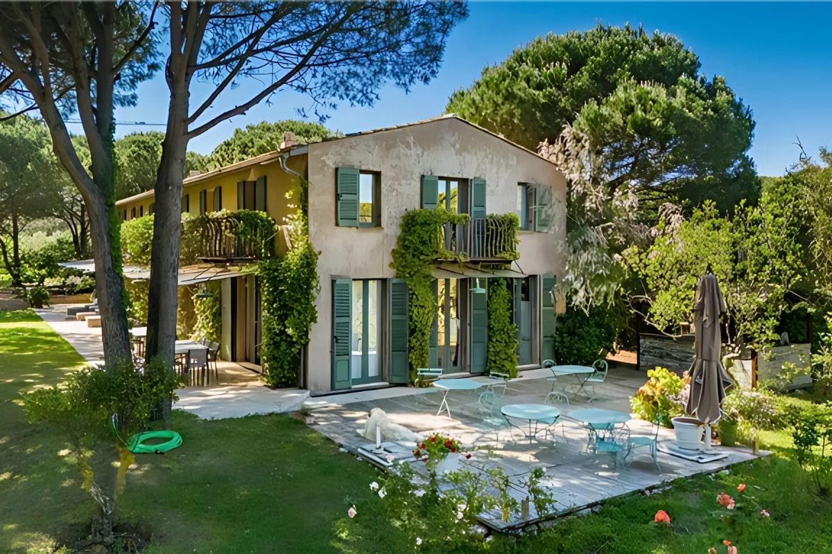 villa-ameline-ramatuelle-rentals-exterior-garden-facade Exterior view of Villa Ameline in Ramatuelle, featuring ivy-covered shutters, a shaded terrace with garden furniture, and a peaceful natural setting.