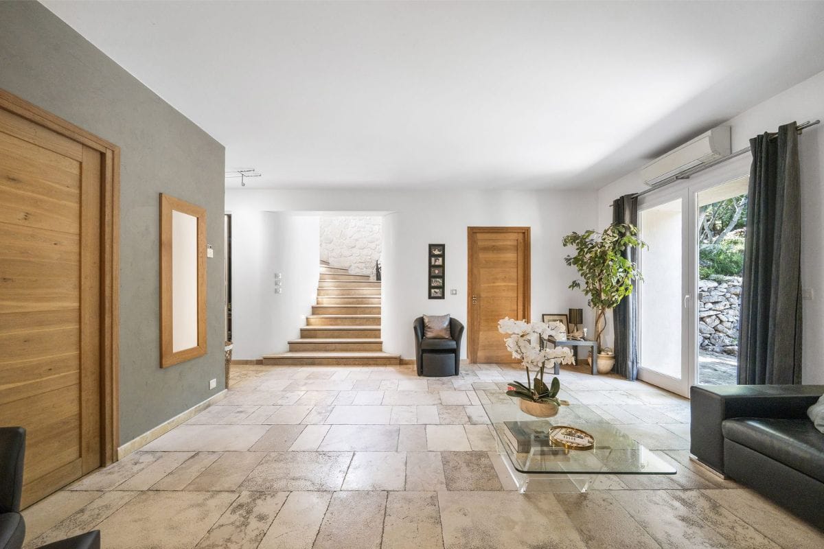 Spacious villa lobby with beige stone tile floor, wooden doors, a staircase to the back, and a glass coffee table in the
